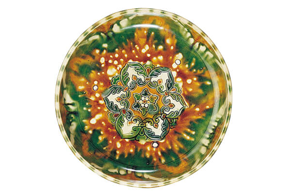 唐代．三彩盤 盤內壓印寶相花紋，表面施以黃、褐、藍、綠、白的釉料，燒成鮮豔華麗的三彩器皿。（圖五）